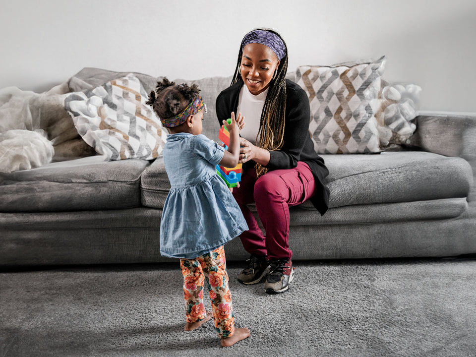 A mother and daughter, both in JUNK headbands, playing with toys together.