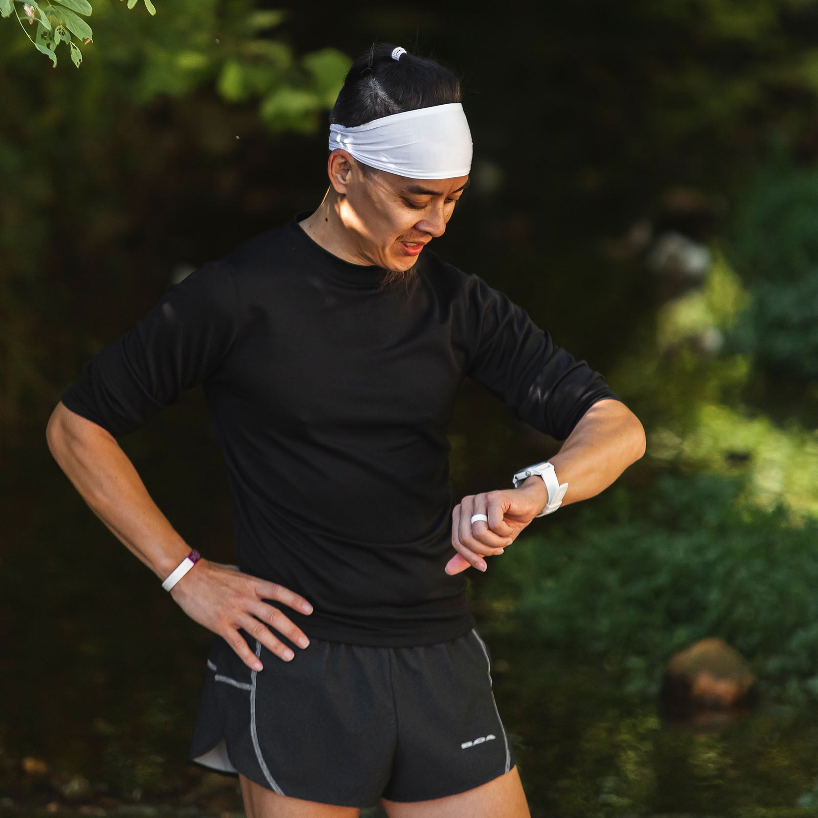 A male runner in a white headband checking his watch.